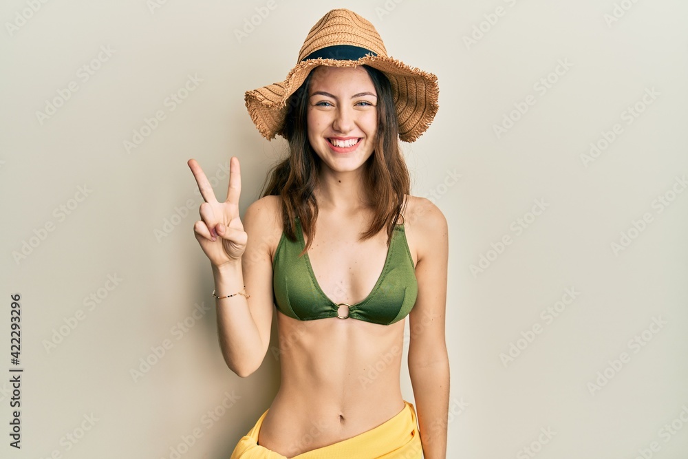 Young brunette woman wearing bikini showing and pointing up with fingers number two while smiling confident and happy. Young brunette woman wearing bikini showing and pointing up with fingers number two while smiling confident and happy.