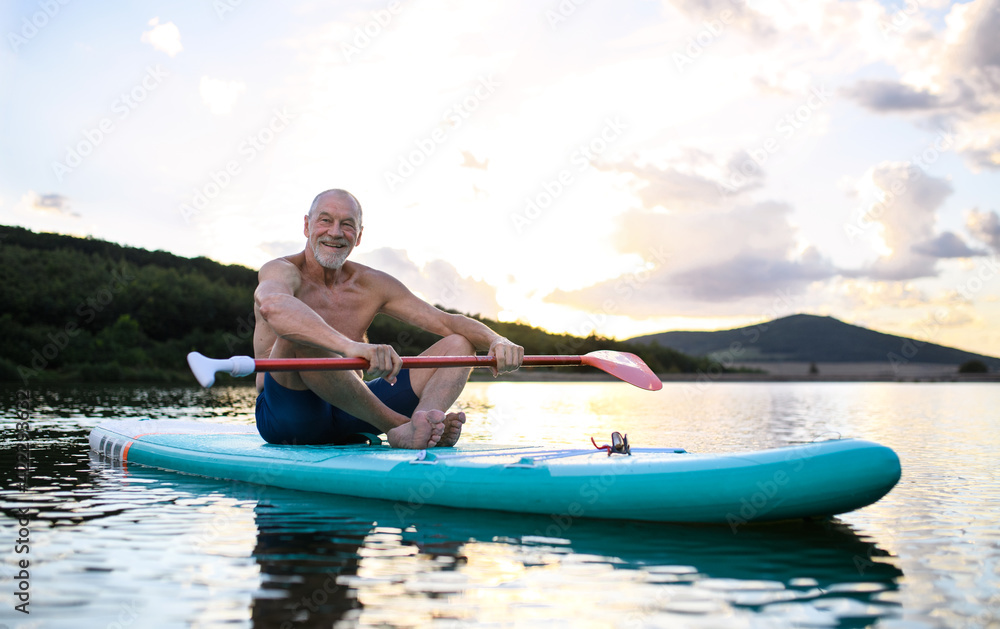 Senior man sitting on paddleboard on lake in summer. Copy space.