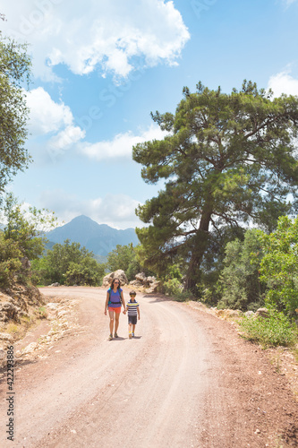 A woman with a backpack walks with her son on a mountain road.