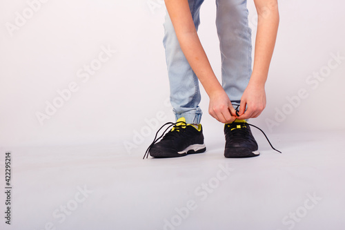 Boy ties shoelaces on sneakers, only hands and feet on white background