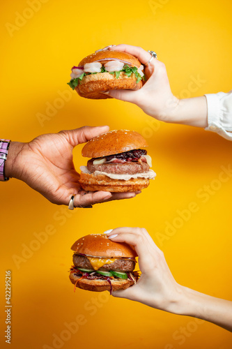 Hands holding burger against yellow background. Fast food, junk food concept.