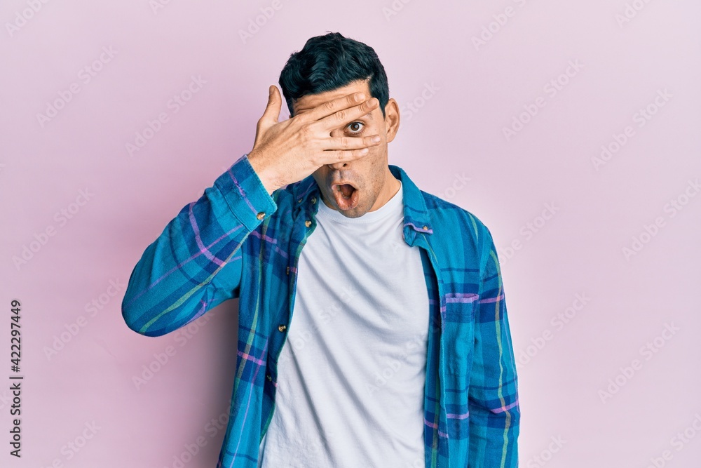 Handsome hispanic man wearing casual clothes peeking in shock covering face and eyes with hand, looking through fingers with embarrassed expression. Handsome hispanic man wearing casual clothes peeking in shock covering face and eyes with hand, looking through fingers with embarrassed expression.
