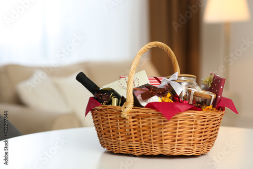 Wicker basket full of gifts on white table in living room photo