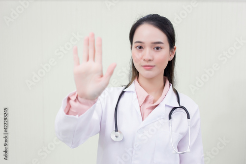 Asian beautiful woman doctor shows hand as stop sign which she wears medical clothing in  health care new normal and coronavirus protection concept.