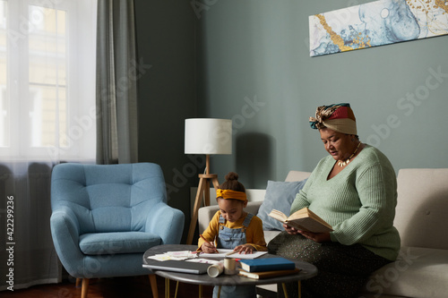 Fotografie Cozy African-American family scene with grandmother reading book while babysitti