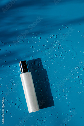 Blue skincare bottle on a blue surface with water drops, natural skincare product for mockup