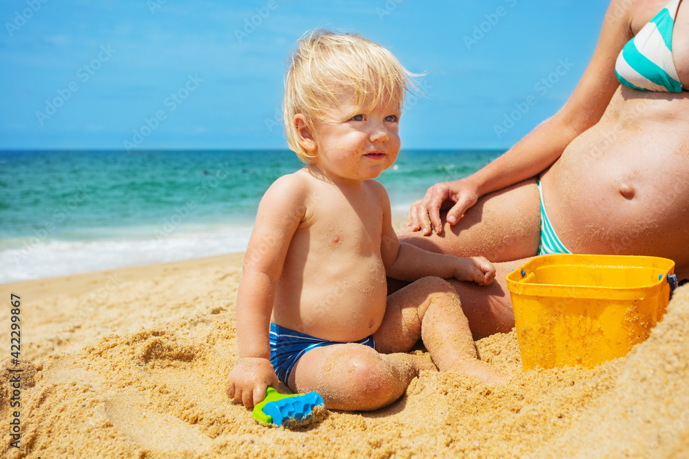 Blond toddler boy with pregnant mother on beach Blond toddler boy with pregnant mother on beach