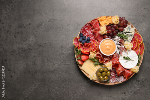 Wooden plate with different delicious snacks on grey table, top view. Space for text