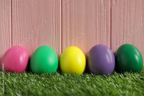 Bright Easter eggs on green grass against pink wooden background
