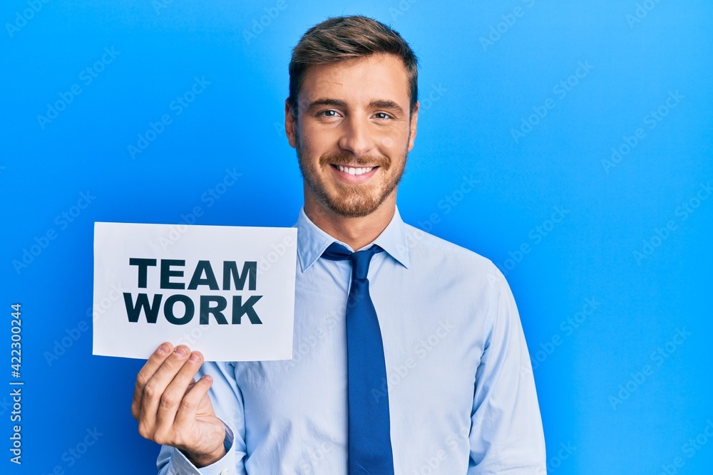 Handsome caucasian business man holding team work banner looking positive and happy standing and smiling with a confident smile showing teeth Handsome caucasian business man holding team work banner looking positive and happy standing and smiling with a confident smile showing teeth