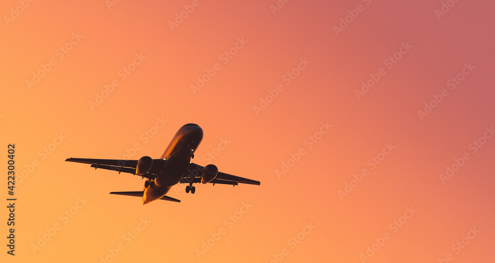 A plane in the sky at sunset. Background, wallpaper with an airplane. Negative space on one sides  (leftward) of the photo. 