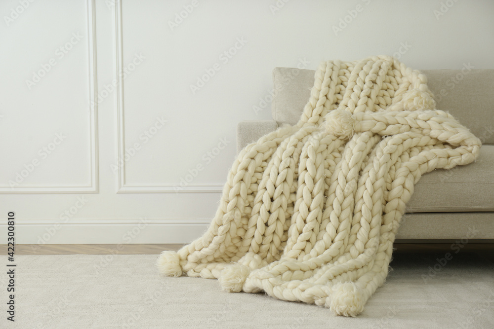 Knitted merino wool plaid on sofa near light wall. Space for text Knitted merino wool plaid on sofa near light wall. Space for text
