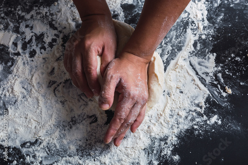 Close-up of hands kneading dough on a black background.