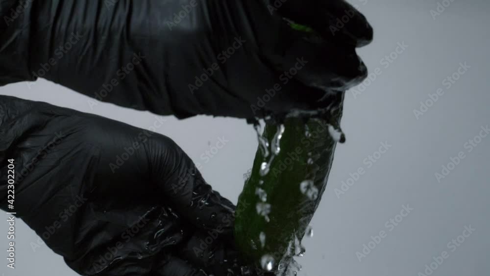 Washing the green cucumber with water splash on grey background. Mans hands in black gloves washing cucumber Washing the green cucumber with water splash on grey background. Mans hands in black gloves washing cucumber