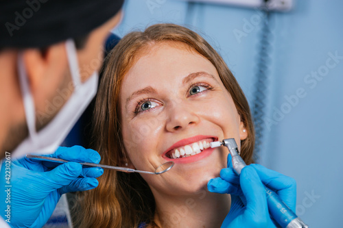 A smiling young woman sits in a dentist's chair while the doctor examines her teeth.