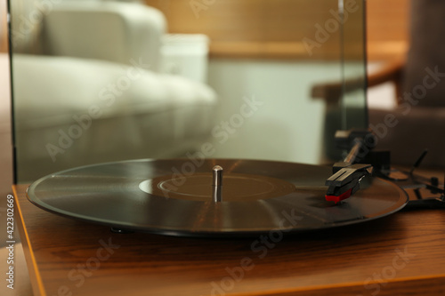 Modern vinyl record player with disc on table indoors, closeup