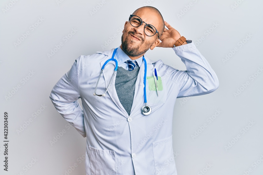Hispanic adult man wearing doctor uniform and stethoscope suffering of neck ache injury, touching neck with hand, muscular pain