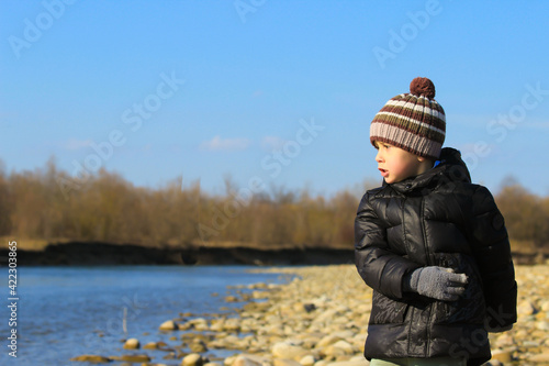 A little boy throws pebbles into the river. Active recreation in nature.