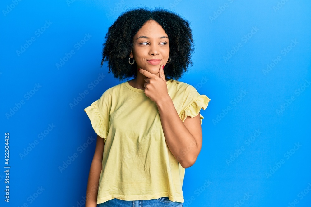 Young african american girl wearing casual clothes with hand on chin thinking about question, pensive expression. smiling with thoughtful face. doubt concept. Young african american girl wearing casual clothes with hand on chin thinking about question, pensive expression. smiling with thoughtful face. doubt concept.