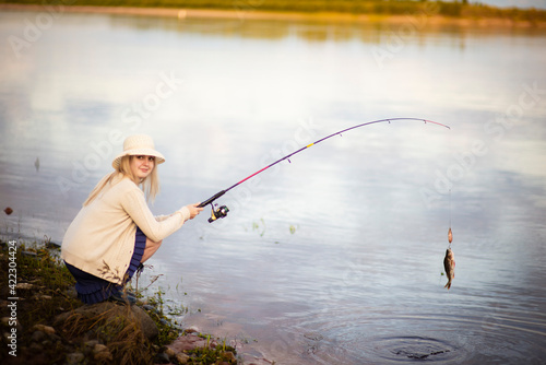 a girl fisherman in a blue dress and hat caught a perch, Selective focus
