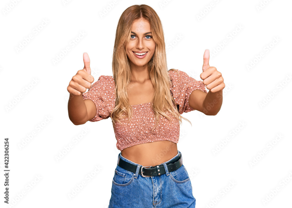 Beautiful blonde young woman wearing summer top approving doing positive gesture with hand, thumbs up smiling and happy for success. winner gesture. Beautiful blonde young woman wearing summer top approving doing positive gesture with hand, thumbs up smiling and happy for success. winner gesture.