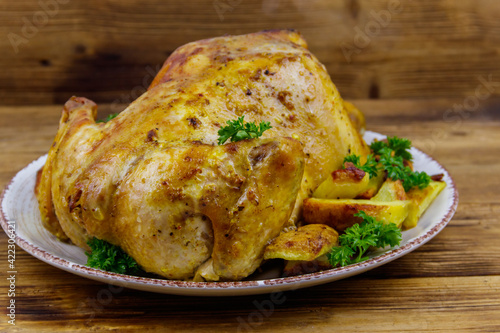 Baked whole chicken with potato on a wooden table