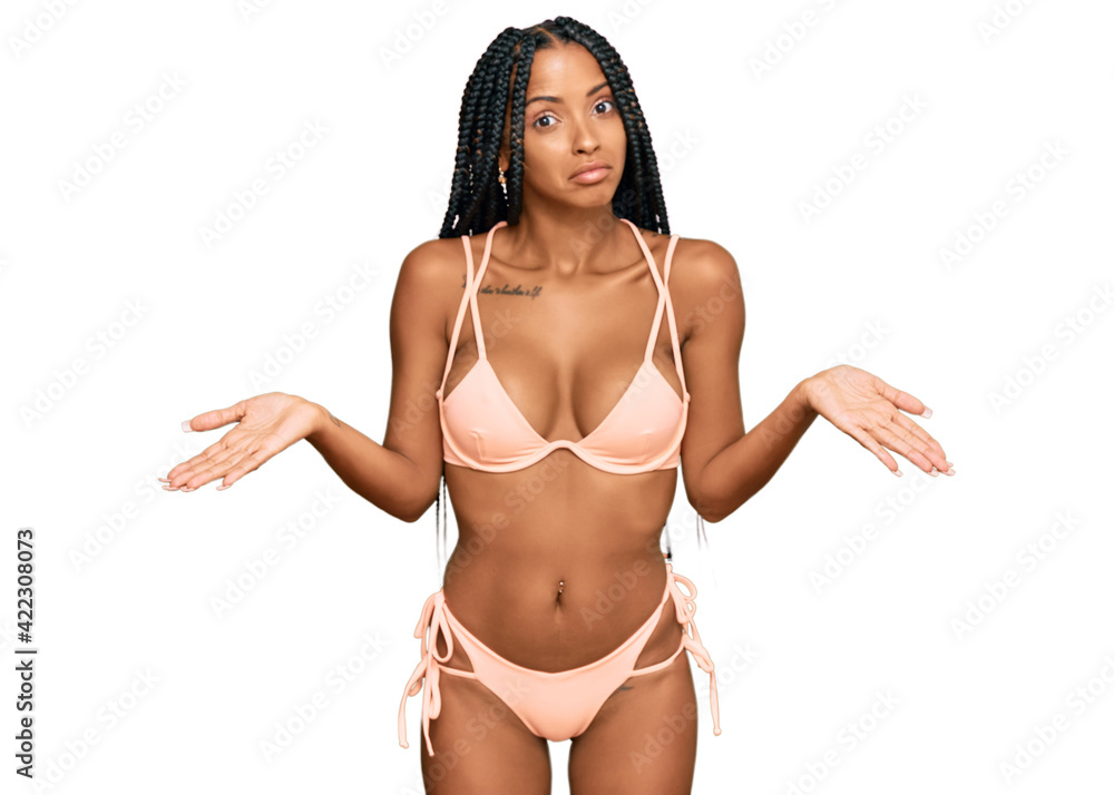 Beautiful hispanic woman wearing bikini clueless and confused expression with arms and hands raised. doubt concept. Beautiful hispanic woman wearing bikini clueless and confused expression with arms and hands raised. doubt concept.