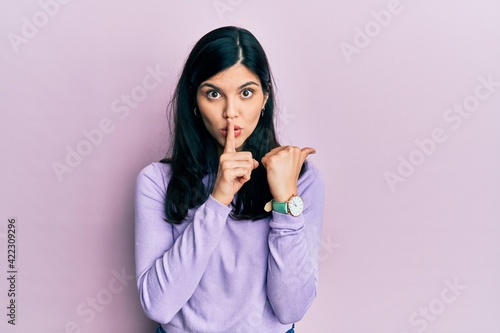 Young hispanic woman wearing casual clothes asking to be quiet with finger on lips pointing with hand to the side. silence and secret concept.