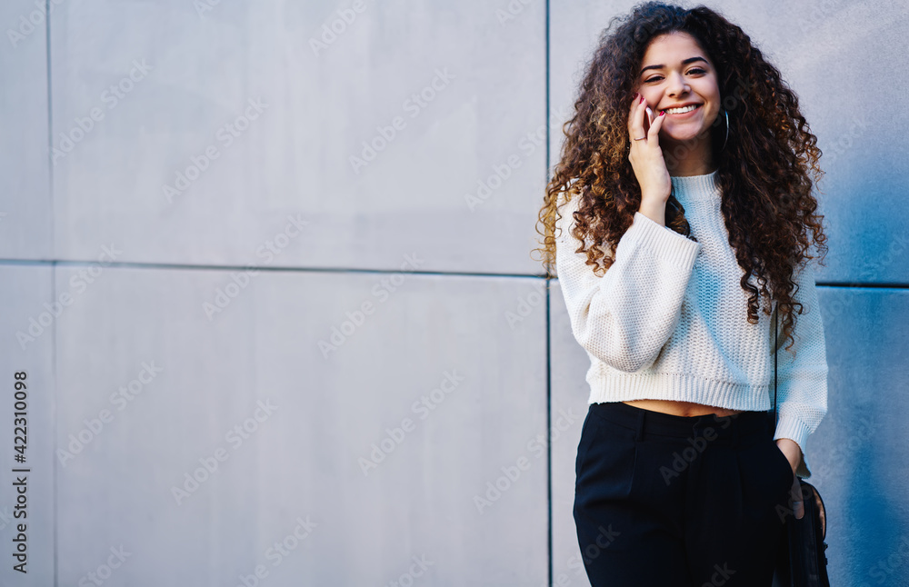 Half length portrait of happy hipster girl with curly hair calling to friend for discussing vacations journey using roaming connection at publicity area with copy space area for operator advertising Half length portrait of happy hipster girl with curly hair calling to friend for discussing vacations journey using roaming connection at publicity area with copy space area for operator advertising