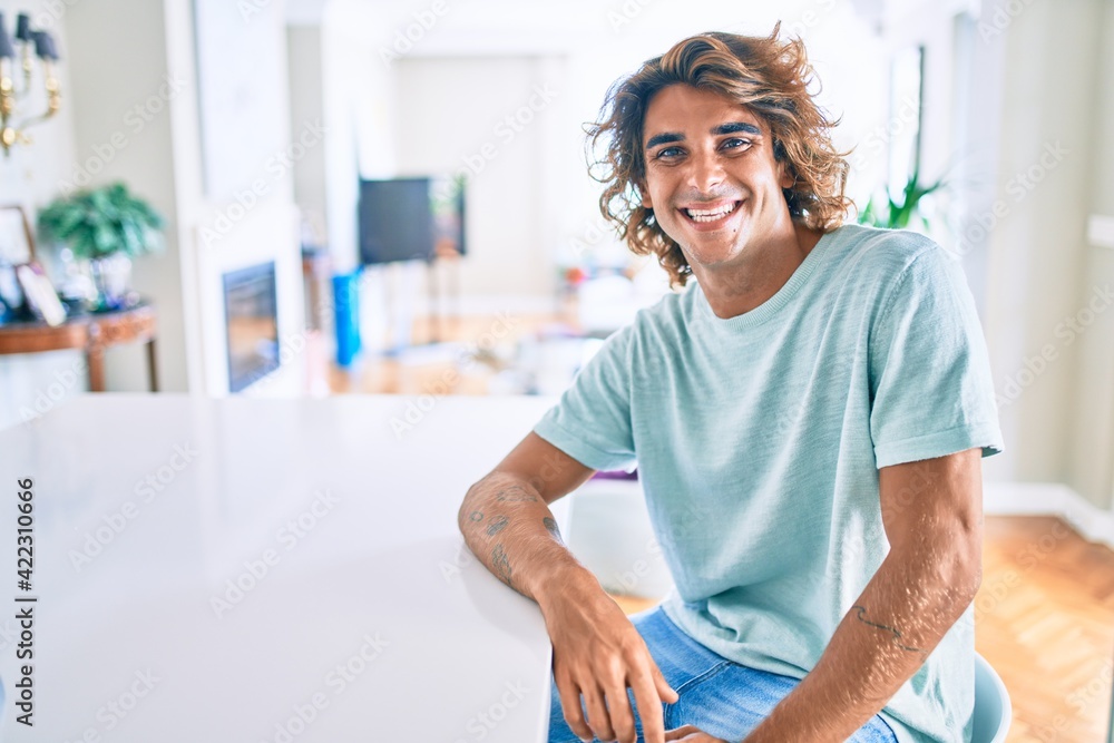 Young hispanic man smiling happy sitting on the table at home Young hispanic man smiling happy sitting on the table at home