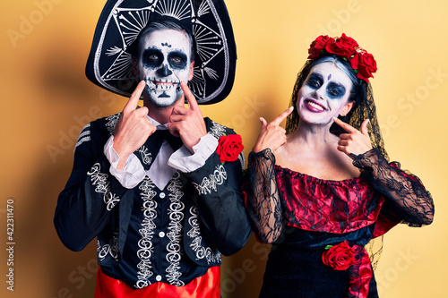 Young couple wearing mexican day of the dead costume over yellow smiling with open mouth  fingers pointing and forcing cheerful smile