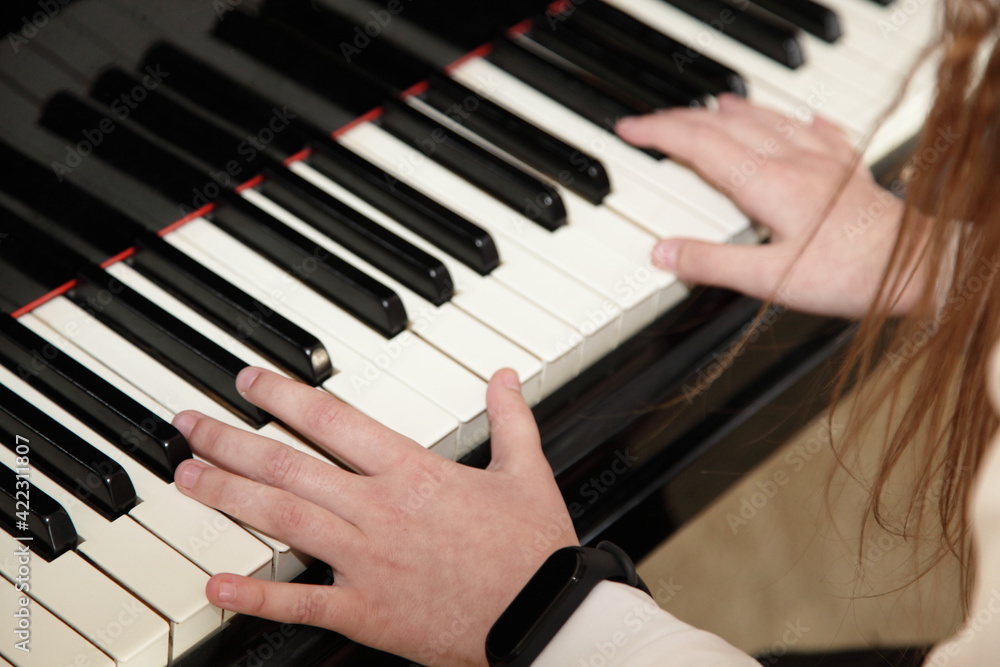 Obraz premium Hands of a white European little pianist girl playing the Grand piano closeup top side view, classic music school education