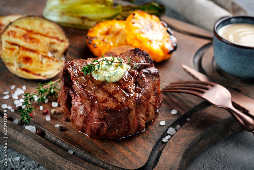 Grilled beef tenderloin steak on a wooden board with butter and thyme. Filet Mignon recipe with vegetables Grilled beef tenderloin steak on a wooden board with butter and thyme. Filet Mignon recipe with vegetables