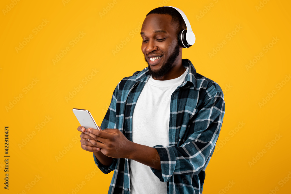 Black Guy Using Smartphone Music App Wearing Headphones, Yellow Background Black Guy Using Smartphone Music App Wearing Headphones, Yellow Background