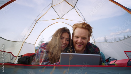 Couple lying in tent with digital tablet. Smiling girl scrolling screen on pad