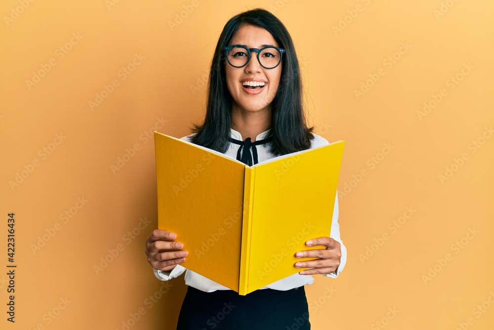 Beautiful asian young woman reading a book wearing glasses smiling and laughing hard out loud because funny crazy joke. Beautiful asian young woman reading a book wearing glasses smiling and laughing hard out loud because funny crazy joke.