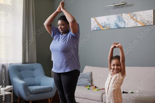 Candid waist up portrait of African-American mother and daughter doing yoga together at home, copy space