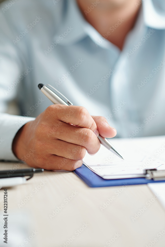Close-up image of businessman sitting at office table and analyzing line chart on clipboard Close-up image of businessman sitting at office table and analyzing line chart on clipboard