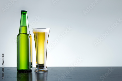 Glass of fresh and cold beer with bootle on grey background with copy space.