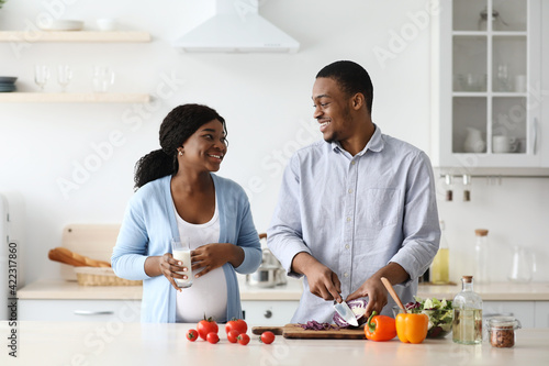 Positive expecting black woman and man cooking healthy food