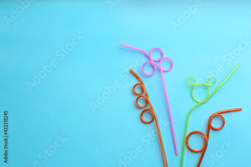 Colorful plastic drinking straws on light blue background, flat lay. Space for text