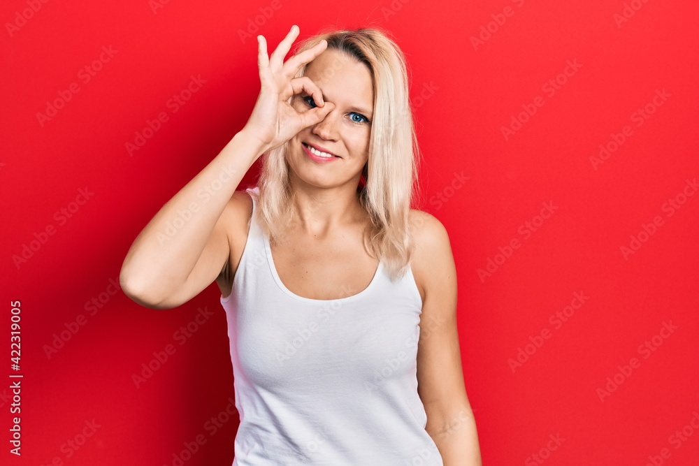 Beautiful caucasian blonde woman wearing casual white t shirt doing ok gesture with hand smiling, eye looking through fingers with happy face.