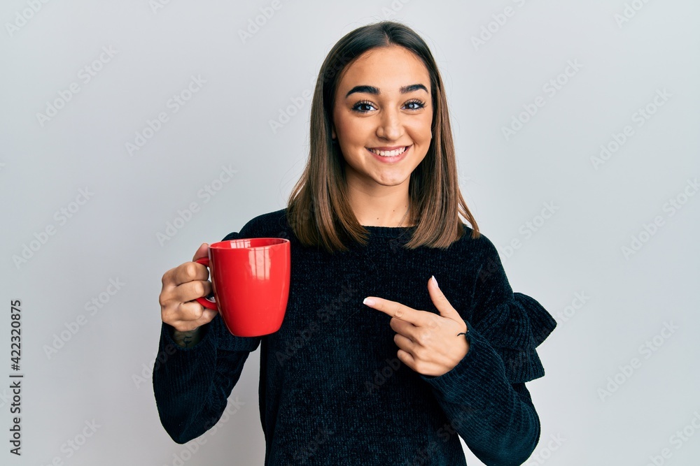 Young brunette girl drinking a cup coffee smiling happy pointing with hand and finger Young brunette girl drinking a cup coffee smiling happy pointing with hand and finger