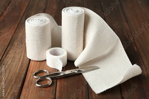 Medical bandage rolls, sticking plaster and scissors on wooden background