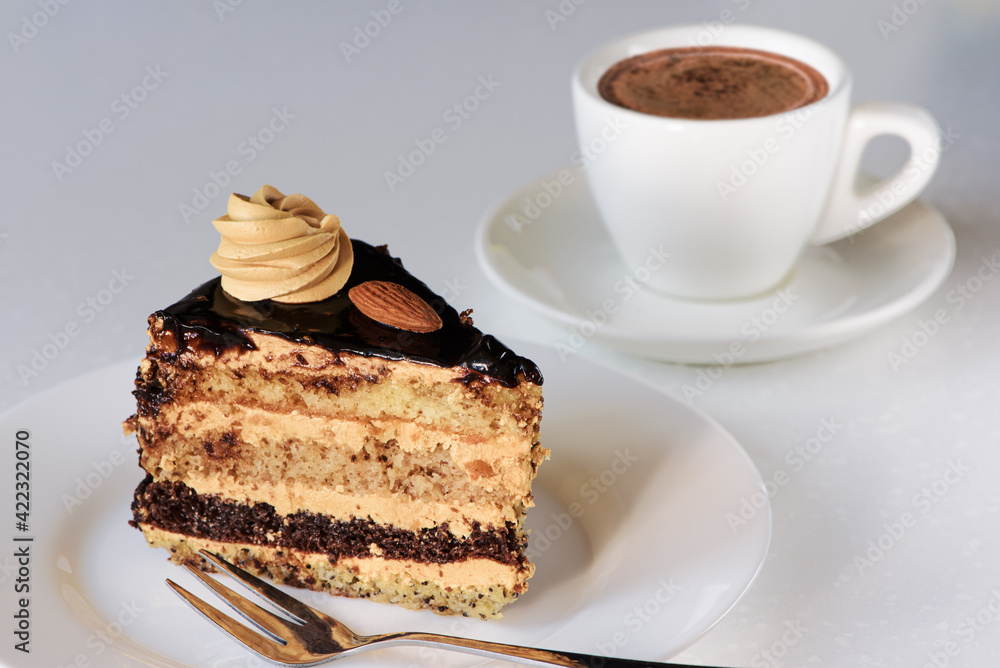 Slice of sponge cake with chocolate icing and cup of coffee on white background. Delicious dessert. Closeup.