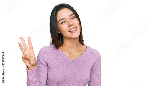 Young hispanic girl wearing casual clothes showing and pointing up with fingers number three while smiling confident and happy.