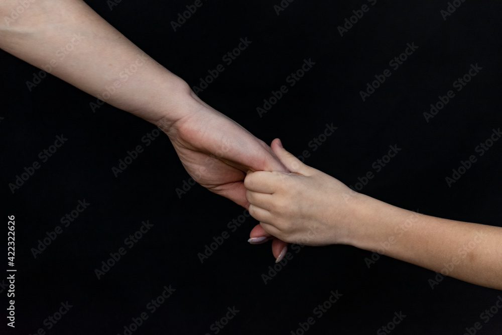 child holding his mother's hand in close-up on a black background.