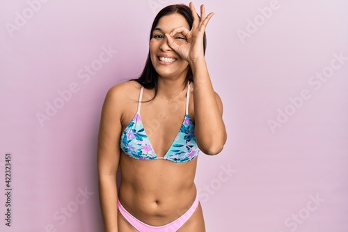 Young latin woman wearing bikini smiling happy doing ok sign with hand on eye looking through fingers © Krakenimages.com