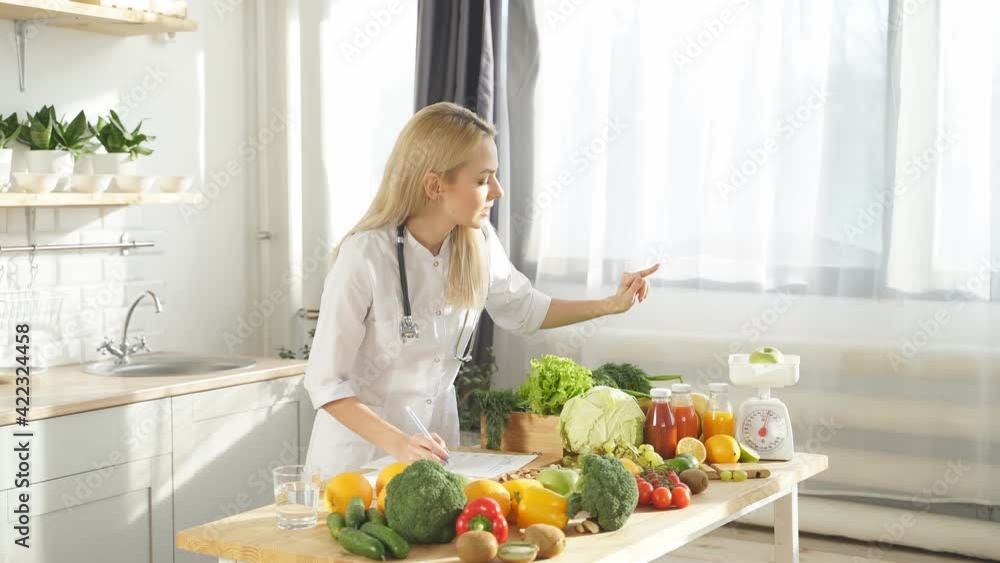 Cute dietitian blogger writes video content about healthy food and healthy eating on her smartphone in her kitchen. Cute dietitian blogger writes video content about healthy food and healthy eating on her smartphone in her kitchen.