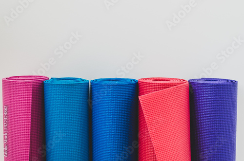 Close up of colourful rolled yoga mats in a yoga studio by a white wall background with copy space